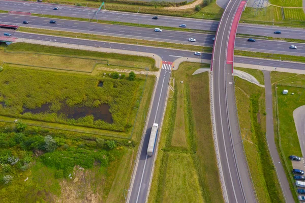 Truck logistic aerial. Trucks motion by the highway intersection road between fields. View from drone.