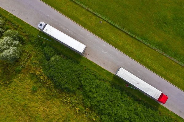 Truck logistic aerial. Two trucks motion by the road between fields. View from drone.