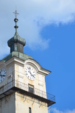 Mavi gökyüzü arka planındaki tarihi kilise kulesinin tepesine yaklaş. Kulede saat ve metal haç var. Gotik mimari. Spisska Sobota, Slovakya