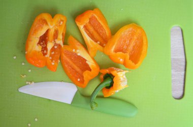 Yeşil kesme tahtasında yeşil seramik bıçakla dilimlenmiş turuncu dolma biber.