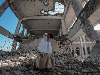 Taiz / Yemen - 23 Aralık 2018: Yemen 'in güneyindeki Taiz kentinde, Houthi milisleri ile ulusal ordu arasında çıkan savaşta harabeye dönüşen okulunun kalıntılarında bir kız oturuyor..