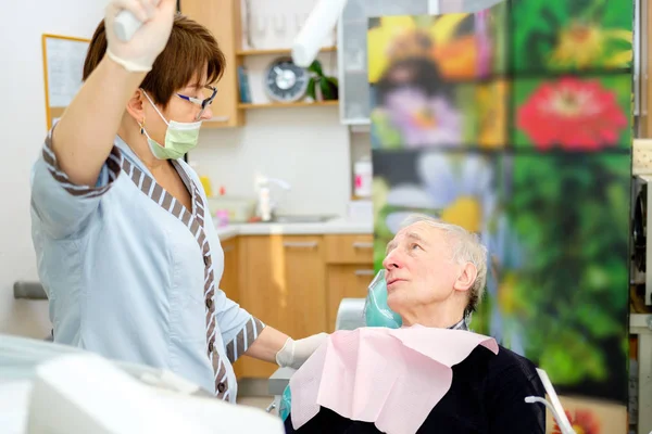 ブルネットの女性歯科医との歯の検査の準備ができて歯科椅子のシニア男性70 75歳の患者の肖像画 高齢者の歯科治療歯科用デバイスを保持する歯科医 — ストック写真