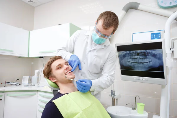 歯科医で歯を検査された歯医者の椅子の若い男 若い男性歯科医 背景のX線 — ストック写真