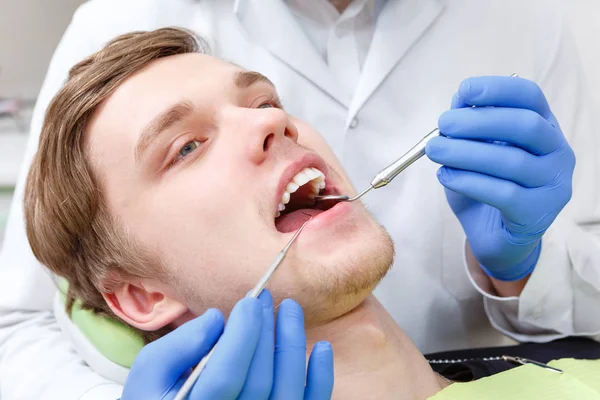 在牙科诊所牙医检查牙齿的牙医坐在牙医椅上的年轻人的特写肖像 — 图库照片