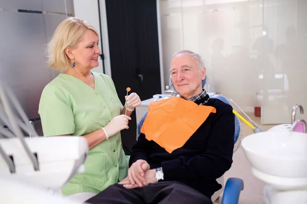 歯科椅子のシニア男性70歳の患者は 素敵なブロンドの女性歯科医と歯の検査の準備ができて — ストック写真