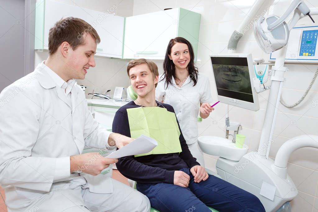 Cheerful smiling male patient and dentist with assistant during check up at dental clinic