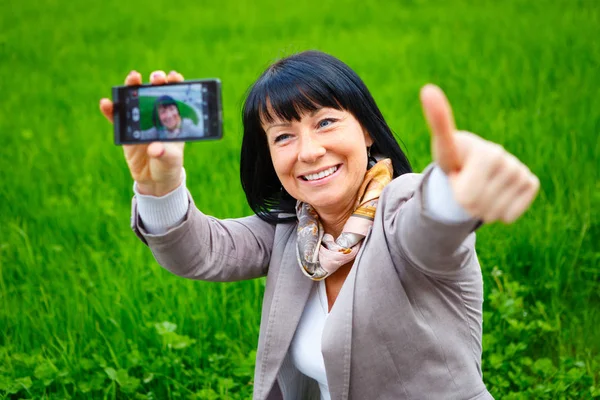 自分撮り 幸せで笑顔の美しい女性35 40歳 緑の草の背景の通りで 夏のジャケットとシルクのスカーフを着て 彼女のスマートフォンの自己の写真を撮りました Instagram — ストック写真