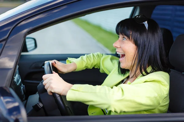 Scared and surprised woman with big eyes holds the steering wheel with both hands shouts driving the car - outdoors