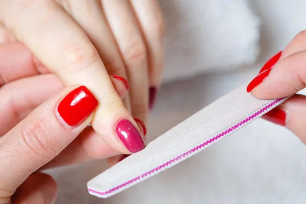 Closeup shot of a woman in a nail salon receiving a manicure by a beautician with nail file. Woman getting nail manicure.