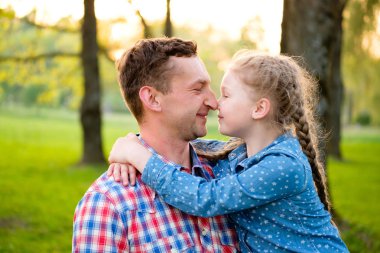 Genç mutlu baba ve kız, doğal yeşil arka planda, yaz parkında yüz yüze eğleniyorlar. Mutlu sevgi dolu aile kavramı