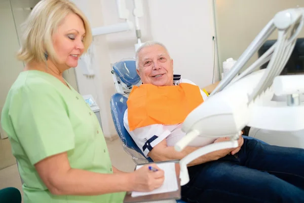 Female dentist talking with smiling senior man patient at dental clinic. Dental care for elder people. Dentistry, medicine and health care concept