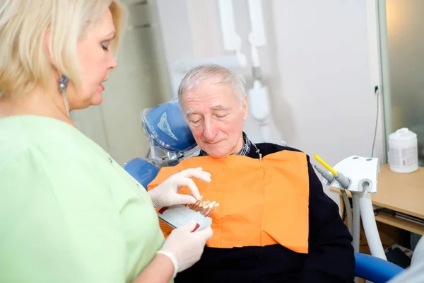 歯科医椅子で70 75歳のシニア男性は 歯の色をチェックして選択します 歯科医は歯科医院で治療のプロセスを行う ヘルスケアの概念 — ストック写真