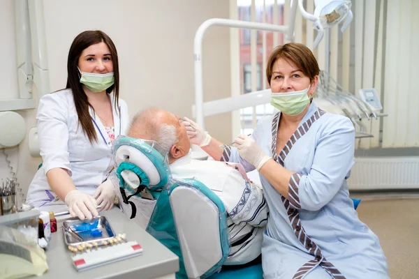 歯科医院で先輩男性患者の歯科治療を行う看護師付き歯科医 高齢者のための歯科治療 ヘルスケアの概念 — ストック写真