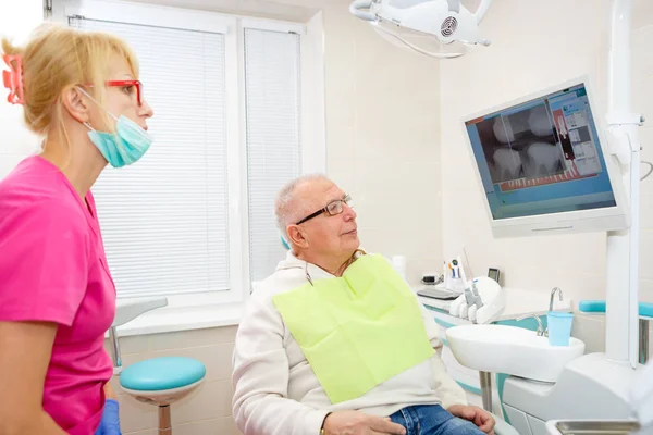 歯科医の見直しで75歳のシニア男性 椅子に座って 年配の男性にX線を説明する歯科医の女性 高齢者のための歯科治療 ヘルスケアの概念 — ストック写真