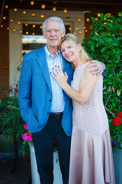 Happy old senior couple in town. Proud Elderly man hugs wife. Summer evening time with backlight