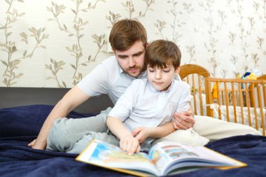 Baba çocuk odasında yatakta oğlu ile birlikte coğrafi kitap okuyor. Kitaba bakmak