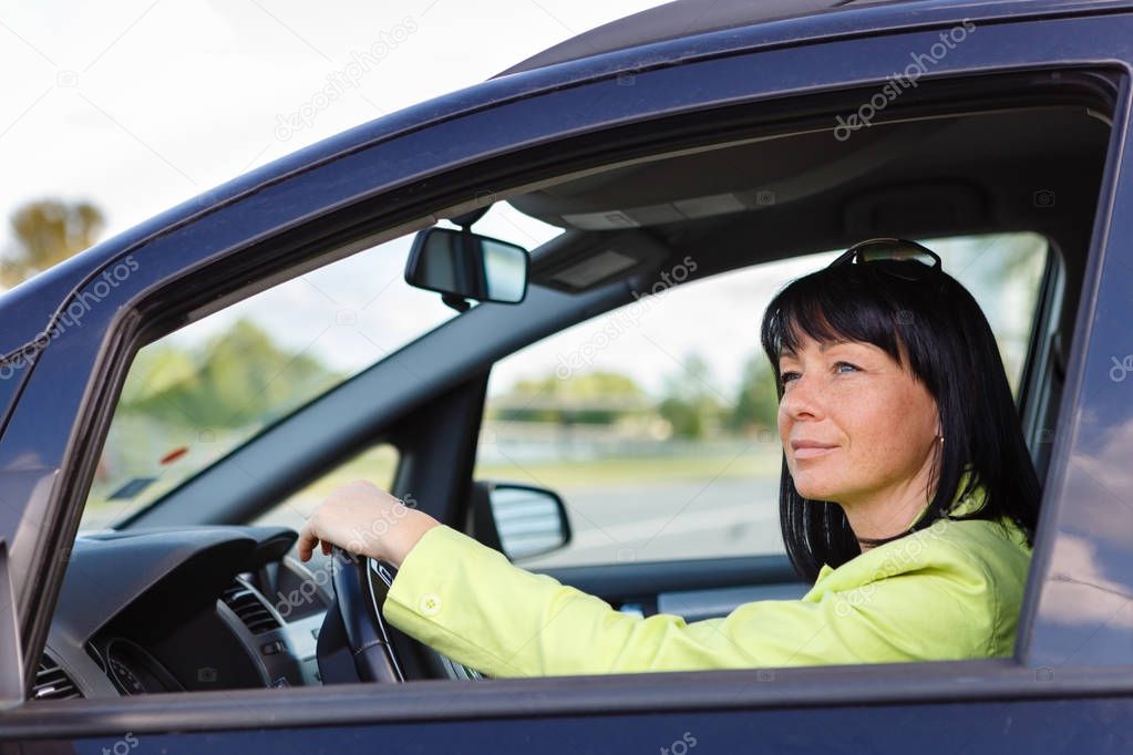 Cute Brunette Woman Sat In The Driver's Seat of Her Car with spring-summer mood. Dressed in green jacket with sun glasses on head