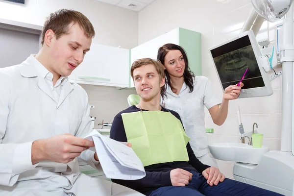 男性患者和牙医在牙科诊所检查牙齿时带助手 — 图库照片