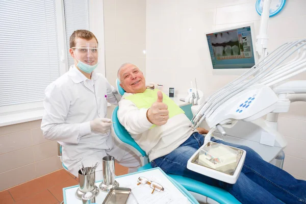 Dentist doctor and old senior man patient showing thumb up smiling and happy looking at camera