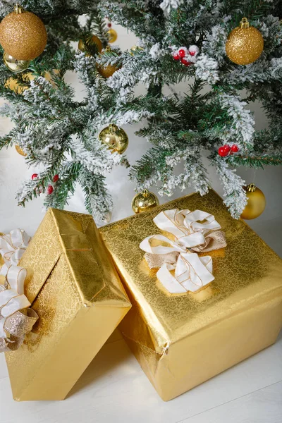 Christmas composition. Xmas tree with gold balls, decorations, toys. White snow on branches. Different size gifts under tree. Gold wrap and pretty bow. Winter holidays card.
