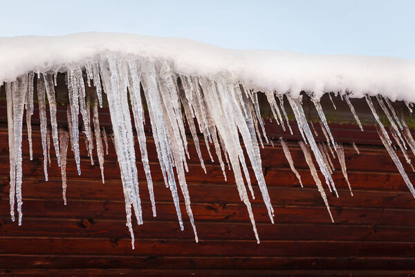 Icicles on the roof. Winter concept. Wood and sky background.