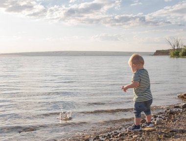 Küçük çocuk suya taş atıyor. Gün batımı. Mutlu çocukluk.
