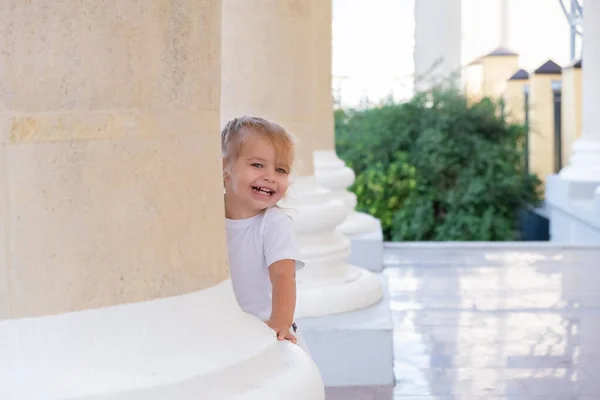 Malá blondýnka dívá zpoza pilíře. — Stock fotografie