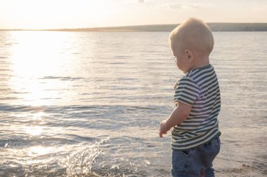 Küçük çocuk suya taş atıyor. Gün batımı. Mutlu çocukluk.