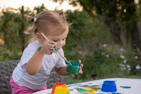 Маленький ребенок рисует краской и кистью. Cute little girl painting picture in garden, outdoors at home in backyard. — стоковое фото