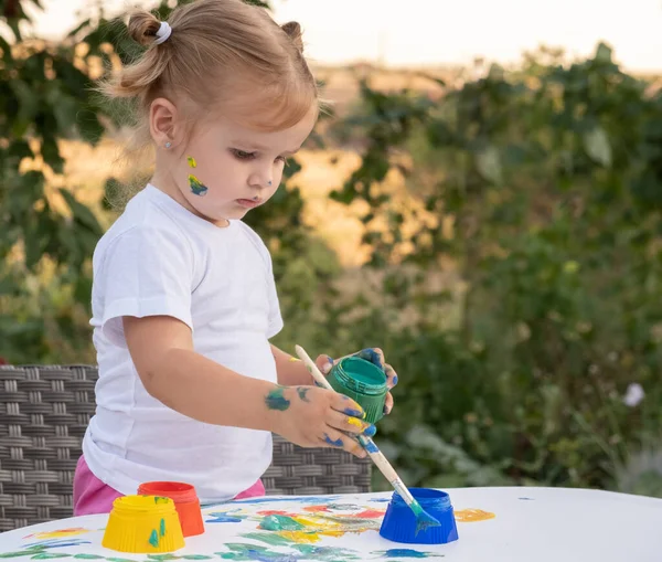 Малышка рисует краской и кистью. на открытом воздухе дома на заднем дворе. — стоковое фото