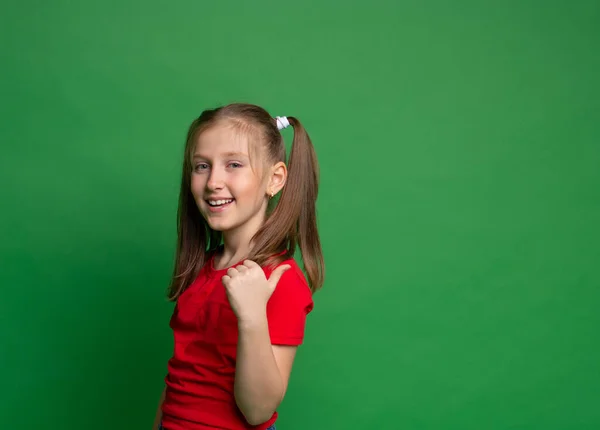 Крупным планом портрет милой молодой девушки, стоящей указывая пальцем, чтобы пустое пространство обратно ее на зеленом фоне — стоковое фото