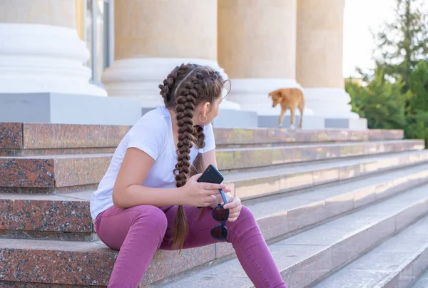 Teenager dívka sedí na schodech drží telefon. — Stock fotografie