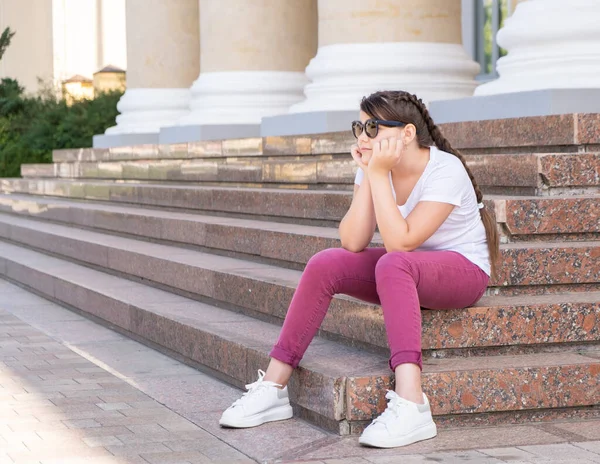 Девочка-подросток в солнцезащитных очках сидит на ступеньках и смотрит в сторону. — стоковое фото