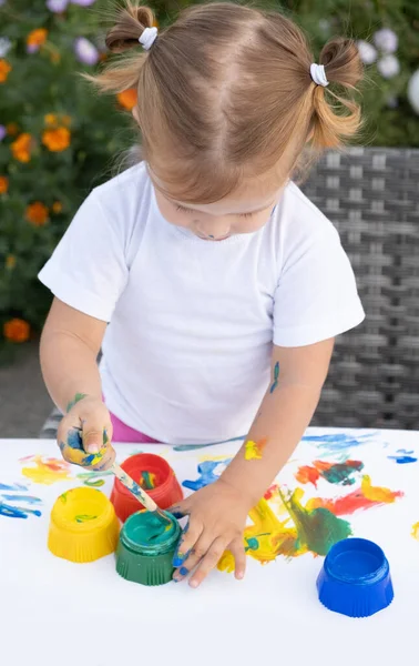 Маленький ребенок рисует краской и кистью. Cute little girl painting picture in garden, outdoors at home in backyard. — стоковое фото