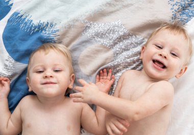 İki küçük ikiz çocuk yatağa uzanıp gülüyor. Yukarıdan bak. Metin için boşluk.