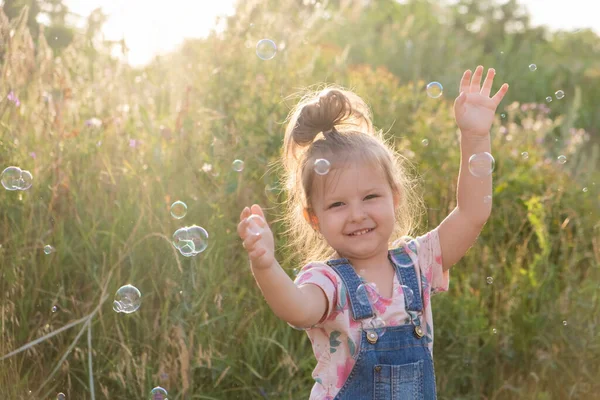 Селективный фокус маленькой милой девочки смеется играя с мыльными пузырями в природе. — стоковое фото