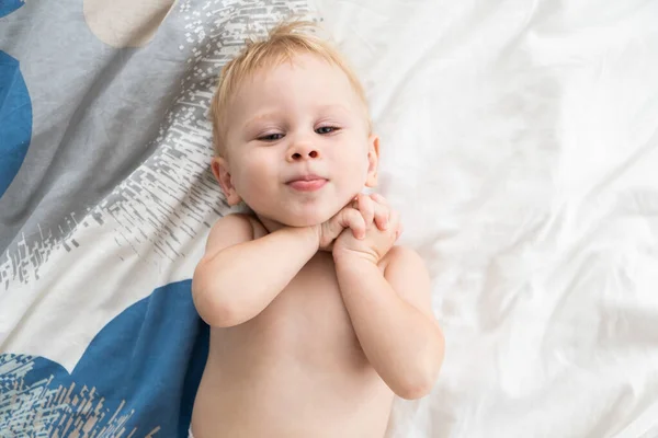 Menino feliz jaz na cama e sorri, vista de cima, espaço para texto. — Fotografia de Stock