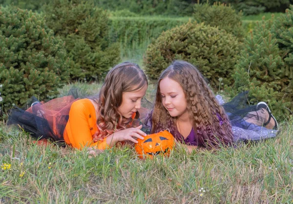 Halloween gyerek lányok jelmez boszorkányok feküdt a füvön Nézi Halloween Candy. — Stock Fotó
