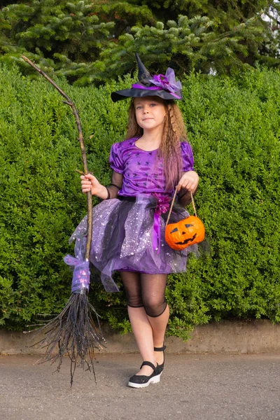 Lány egy lila boszorkány jelmez narancs tök és seprű. — Stock Fotó