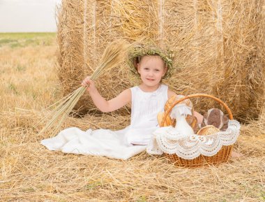 Küçük sarışın kız elinde ekmek ve sütle samanlıkta oturuyor. Çevre dostu tarım ürünleri.