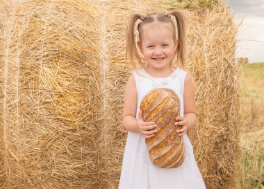 Beyaz elbiseli küçük sarışın kız tarlada ekmek tutuyor. Çevre dostu tarım ürünleri.
