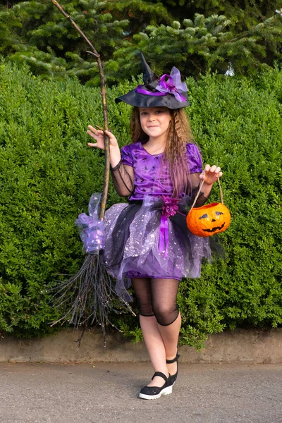 Menina em um traje de bruxa roxo com abóbora laranja e vassoura. — Fotografia de Stock