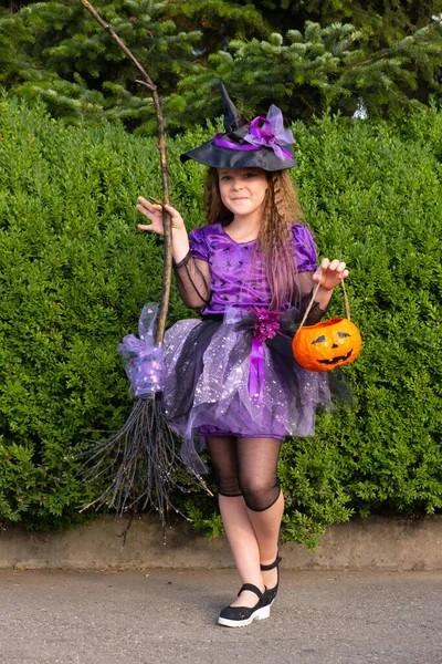 Fille dans un costume de sorcière pourpre avec citrouille orange et balai. — Photo