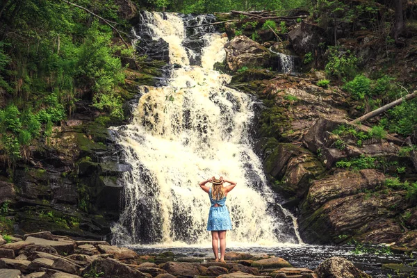 Orman şelalesi yakınlarında doğanın tadını çıkaran şapkalı bir kadın. Rahatlama ve özgürlük hissi..
