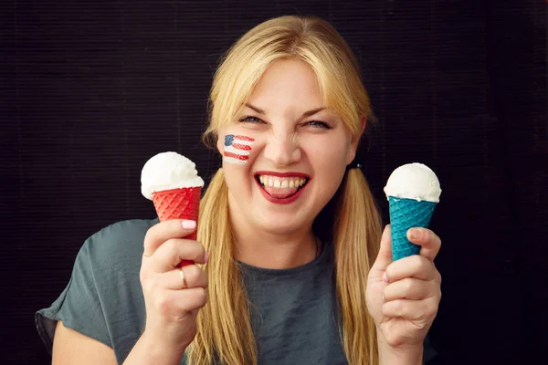アイスクリームを食べる彼女の顔の上にアメリカ国旗を持つ少女 私たちの独立記念日 — ストック写真