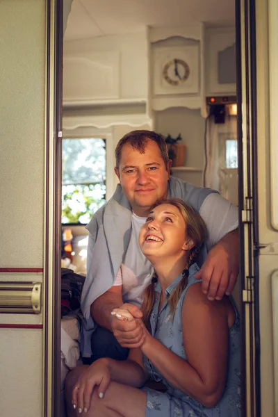 Happy couple of tourists sitting in a camper van on a summer day.
