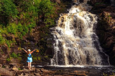 Buket çiçek yakınındaki bir orman şelale ile şapkalı kadın. Gevşeme ve özgürlük hissi.