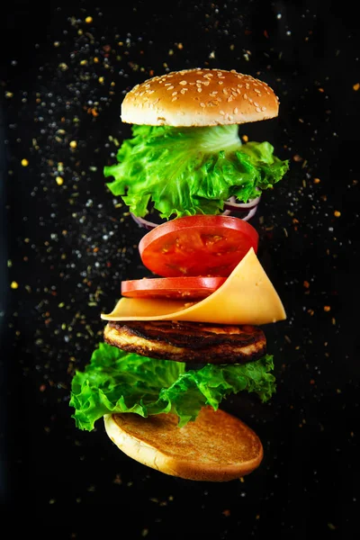 Siyah bir arka plan üzerinde bir ev yapımı burger için Uçan malzemeler. 