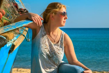 Kumsalda yaşlı balıkçı teknesinin yanında çekici yalnız bir kız..