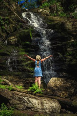 Orman şelalesi yakınlarında doğanın tadını çıkaran şapkalı bir kadın. Rahatlama ve özgürlük hissi..